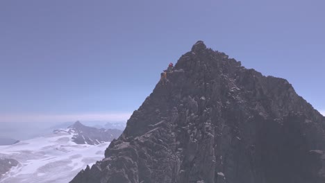 Mountaineer-on-summit-ridge-approaching-high-elevation-peak-with-glaciers-in-background