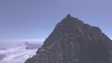 montañero en cumbre ridge acercándose a pico de gran elevación con glaciares en segundo plano.