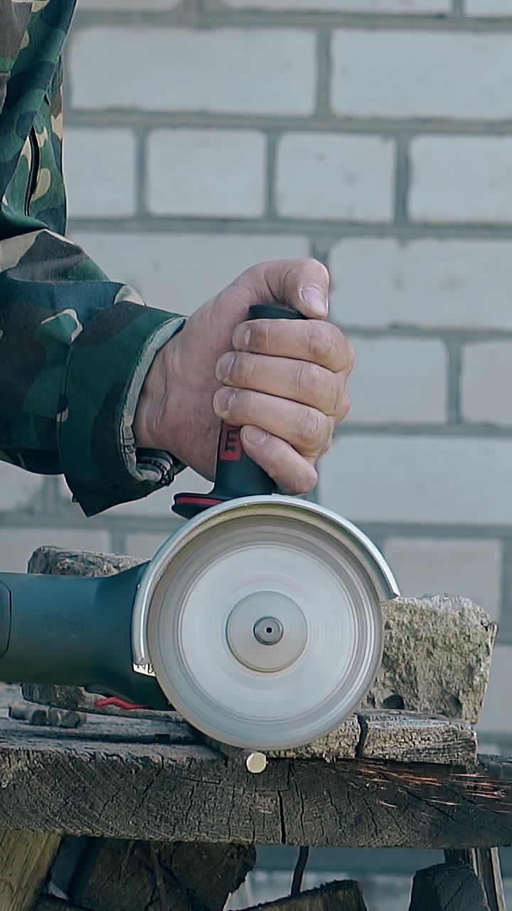 skilled builder in work wear cuts metal rod using hand disc saw on table against white brick wall