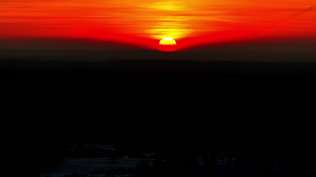 Eine feuerrote Sonne geht unter dem dunklen Horizont unter und taucht den Himmel in tiefes Orange und Karminrot – Weitwinkel-Luftaufnahme.