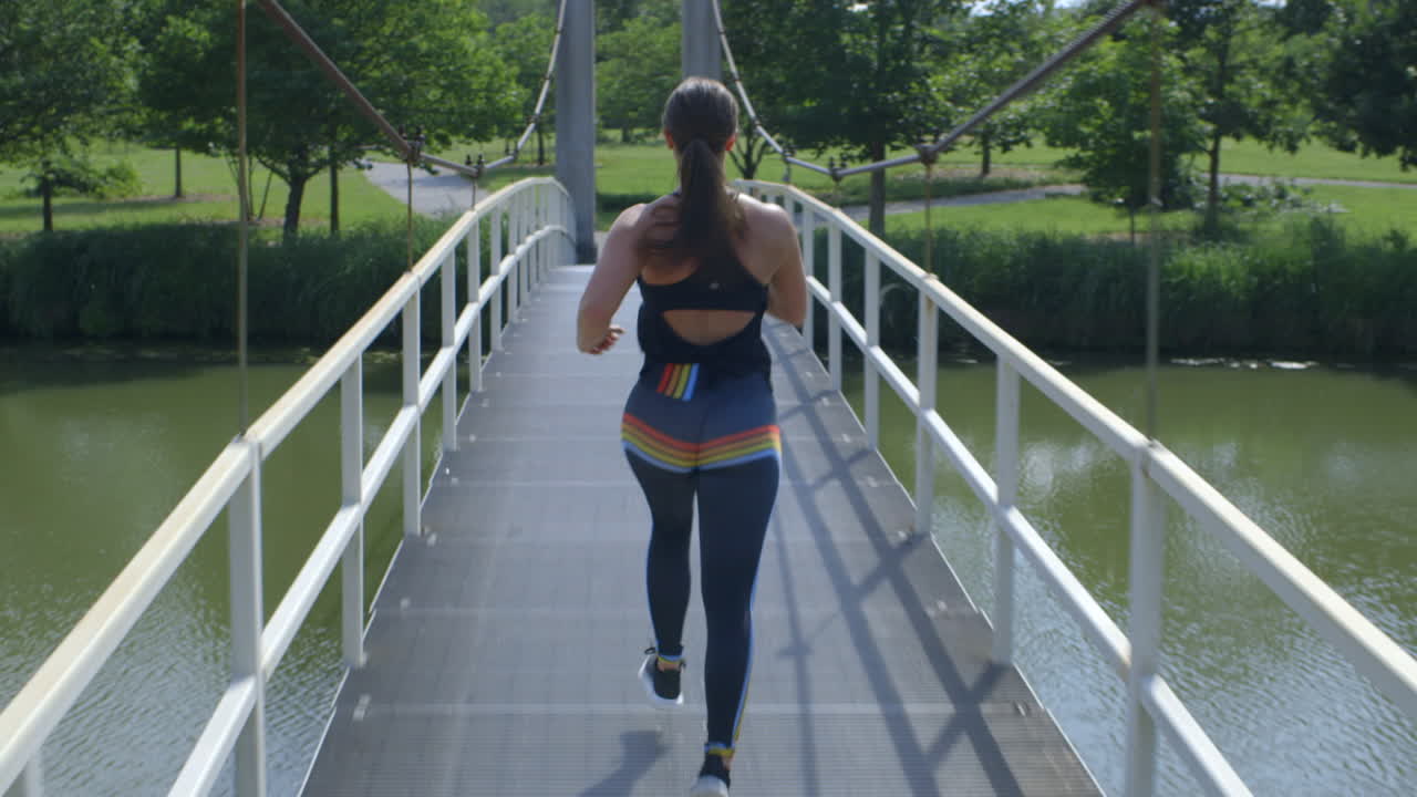 una mujer cruza un puente levadizo en un parque forestal en verano con la cámara detrás de ella