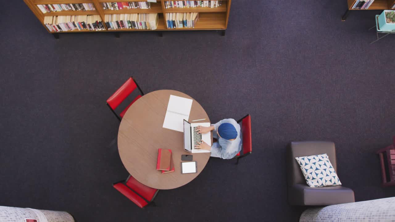 Asian female student wearing a blue hijab sitting and using a laptop