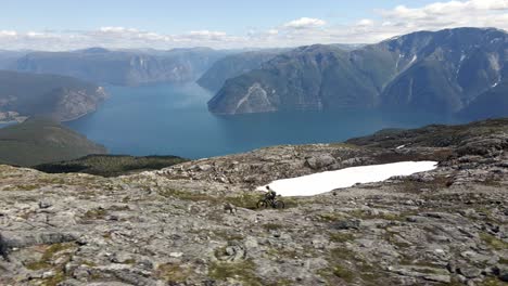 spectacular drone shot showing mountain biker riding on rocky summit of norwegian mountains - beautiful valley with blue fjord in summer