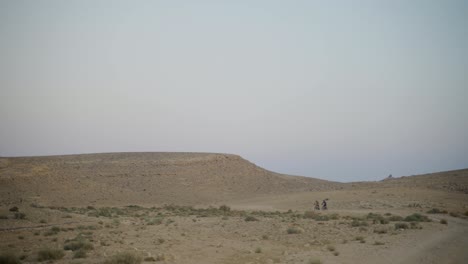 mountain bike riders in the distance cycle next to desert hill