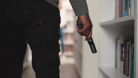 man with gun prepares attack on public library closeup. african american guy holds handgun walking across literature storage. criminal actions