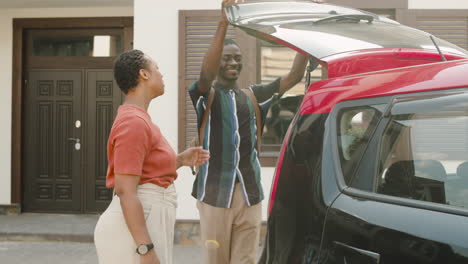 young man and his mom standing outside next to car, hugging and saying goodbye before boy moving home