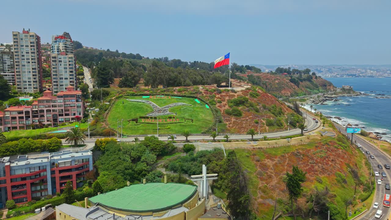 Volo di drone aereo con bandiera cilena, traffico stradale costiero ed edifici del resort a Reñaca, Viña del Mar, Cile