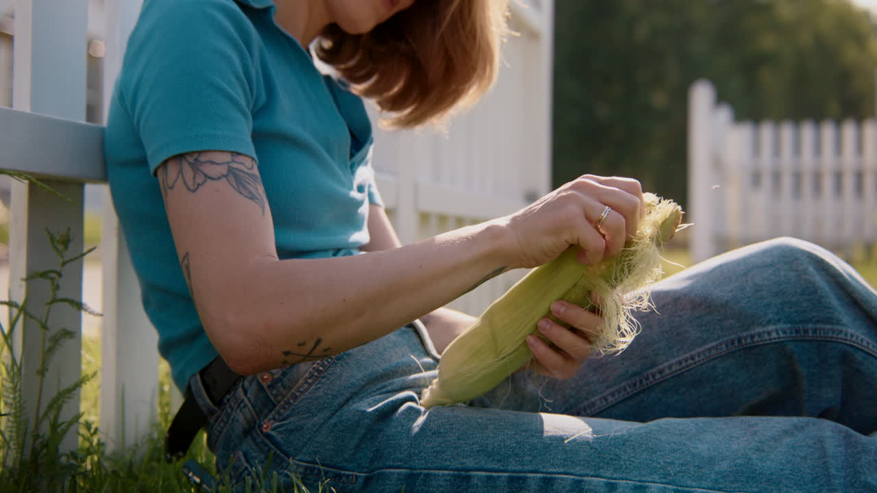Woman eating corn by a white picket fence