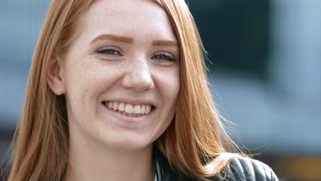 A-beautiful-optimistic-young-red-haired-woman-looks-at-the-camera-and-smiles-sweetly-in-the-city
