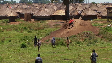 longshot of young children run and playing in a village or refugee camp in northern uganda