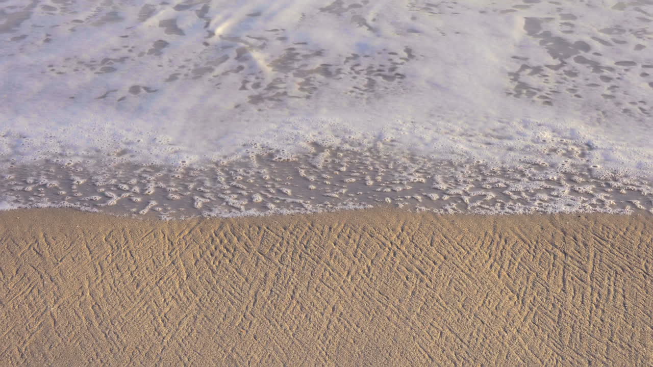 Skummende bølger slår mod strandsandet ved daggry. - slowmotion, zenital vinkel