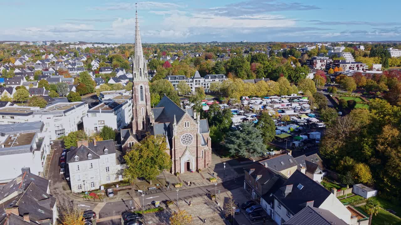 Church of Saint Martin tower stands over surrounding neighborhood with bright daylight revealing rooftops and trees, Cesson Sevigne, Brittany in France