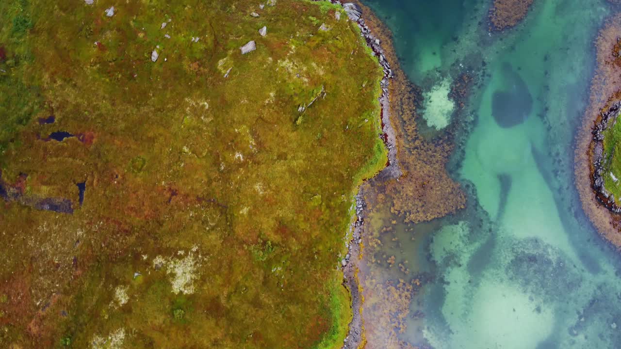 Drone aerial footage flying over bright blue turquoise water of the sea surrounded by the autumn colours of the landscape beneath it in northern Norway