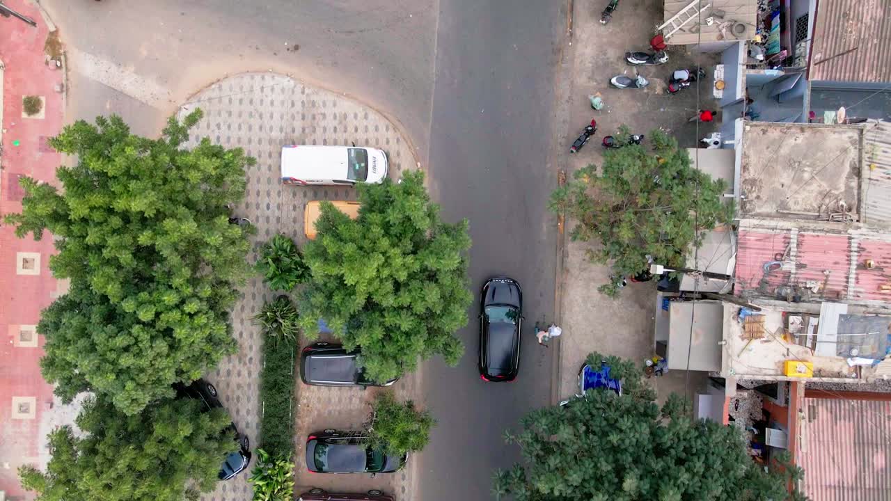 Aerial drone footage of a black car cruising along a road in Dakar, Senegal. The camera smoothly follows the vehicle, revealing the dynamic landscape, urban textures, and a strong sense of motion