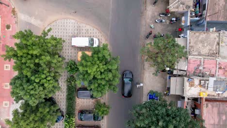 aerial drone footage of a black car cruising along a road in dakar, senegal. the camera smoothly follows the vehicle, revealing the dynamic landscape, urban textures, and a strong sense of motion