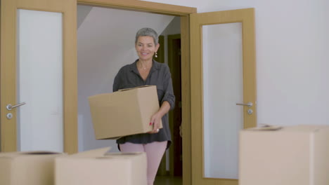 Happy beautiful mature woman entering new house with cardboard boxes