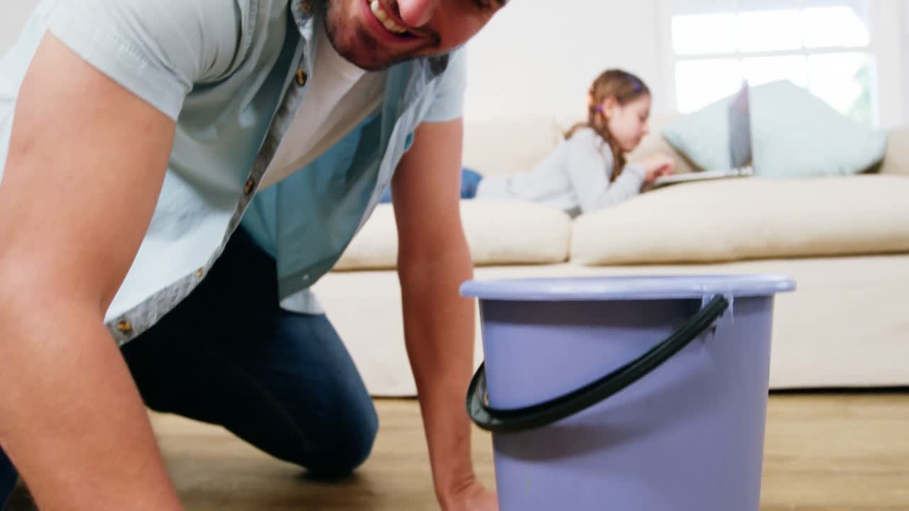 Man cleaning the floor while daughter using digital tablet