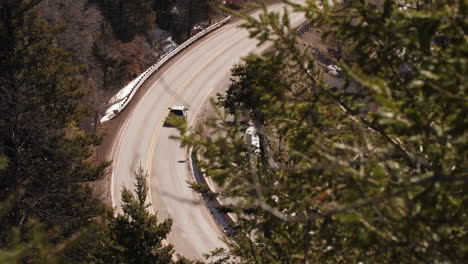 An-SUV-drives-along-a-winding-mountain-road-in-the-forest,-long-lens