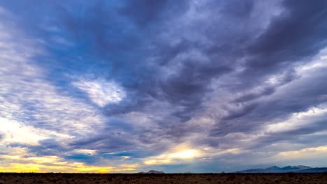 the golden colors of a mojave desert sunset illuminate the sky in this harsh wilderness with mountains in the distance - time lapse cloudscape