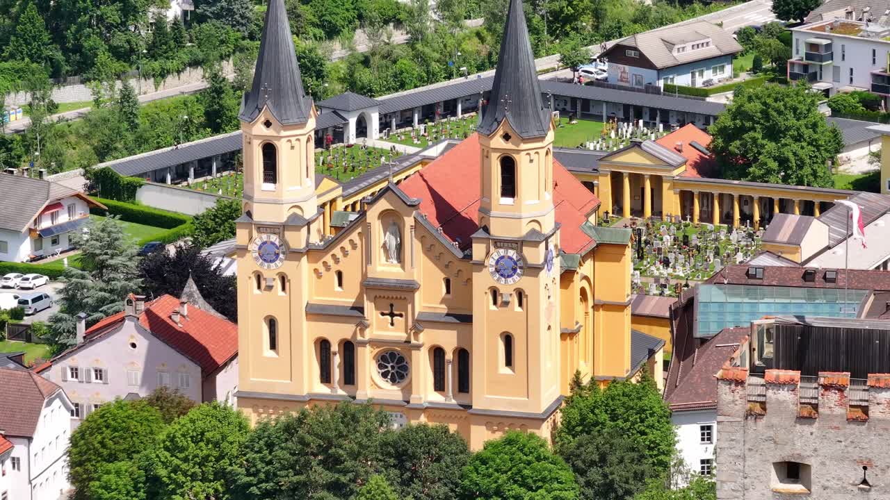 A yellow church with twin spires in bruneck on a sunny day, aerial view