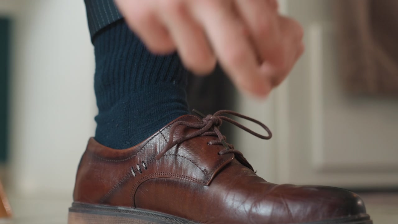 Close-up sepatu kulit cokelat diikat dengan cepat, pria bergegas ke kantor, jari-jari cekatan mengikat tali sepatu, sol yang lecet, koridor dalam ruangan, celana jas terlihat, suasana hati yang tepat waktu, energi pagi perkotaan