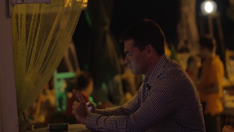 man with mobile phone in street cafe at night