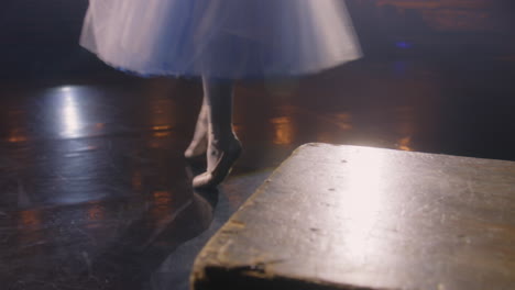 ballerina puts on pointe shoes for choreography rehearsal. ballet female dancer practices before performance and dances on tiptoe on theater stage illuminated by spotlights. classical ballet dance.