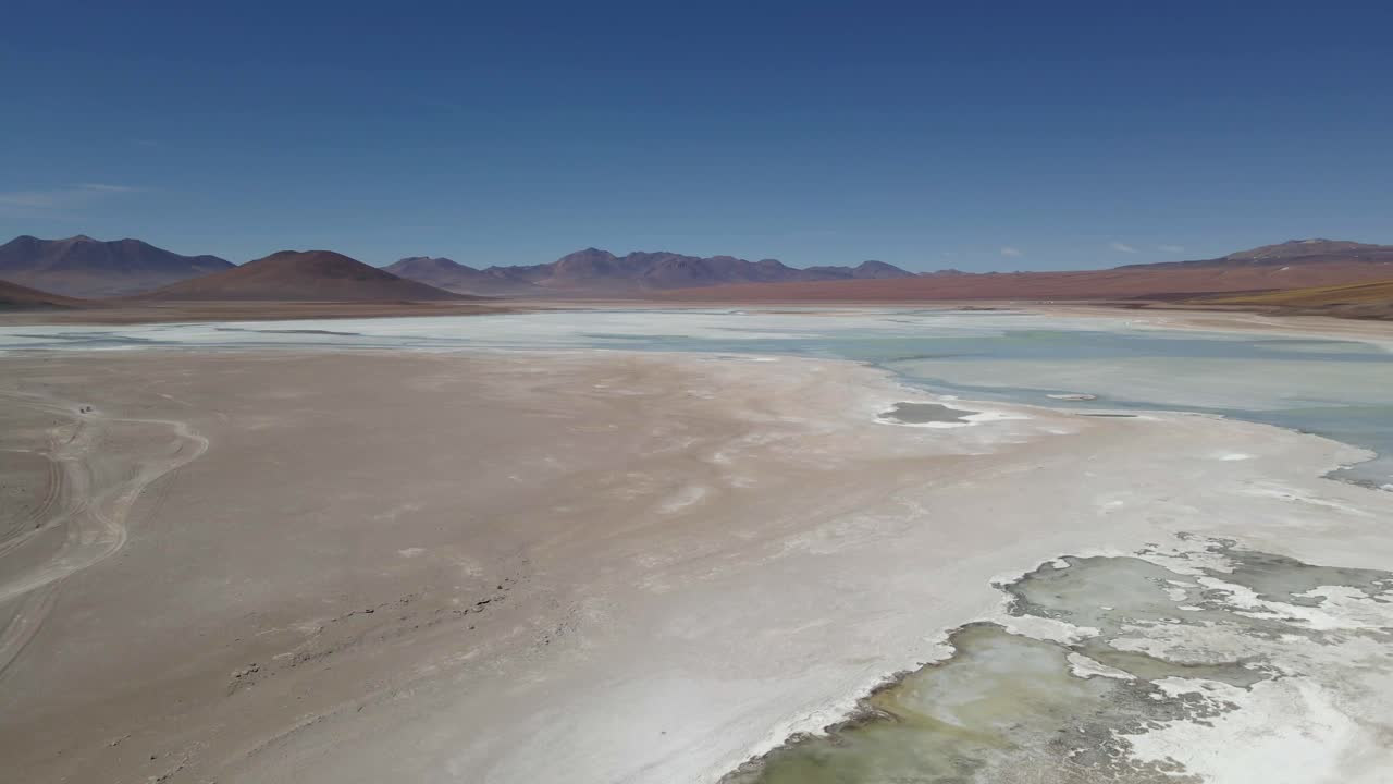 Drone orbits over white lake with visible mineral layers in southern Bolivia under blue sky