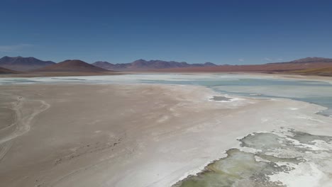 drone orbits over white lake with visible mineral layers in southern bolivia under blue sky