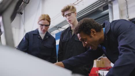 male tutor with students looking at car engine on auto mechanic apprenticeship course at college