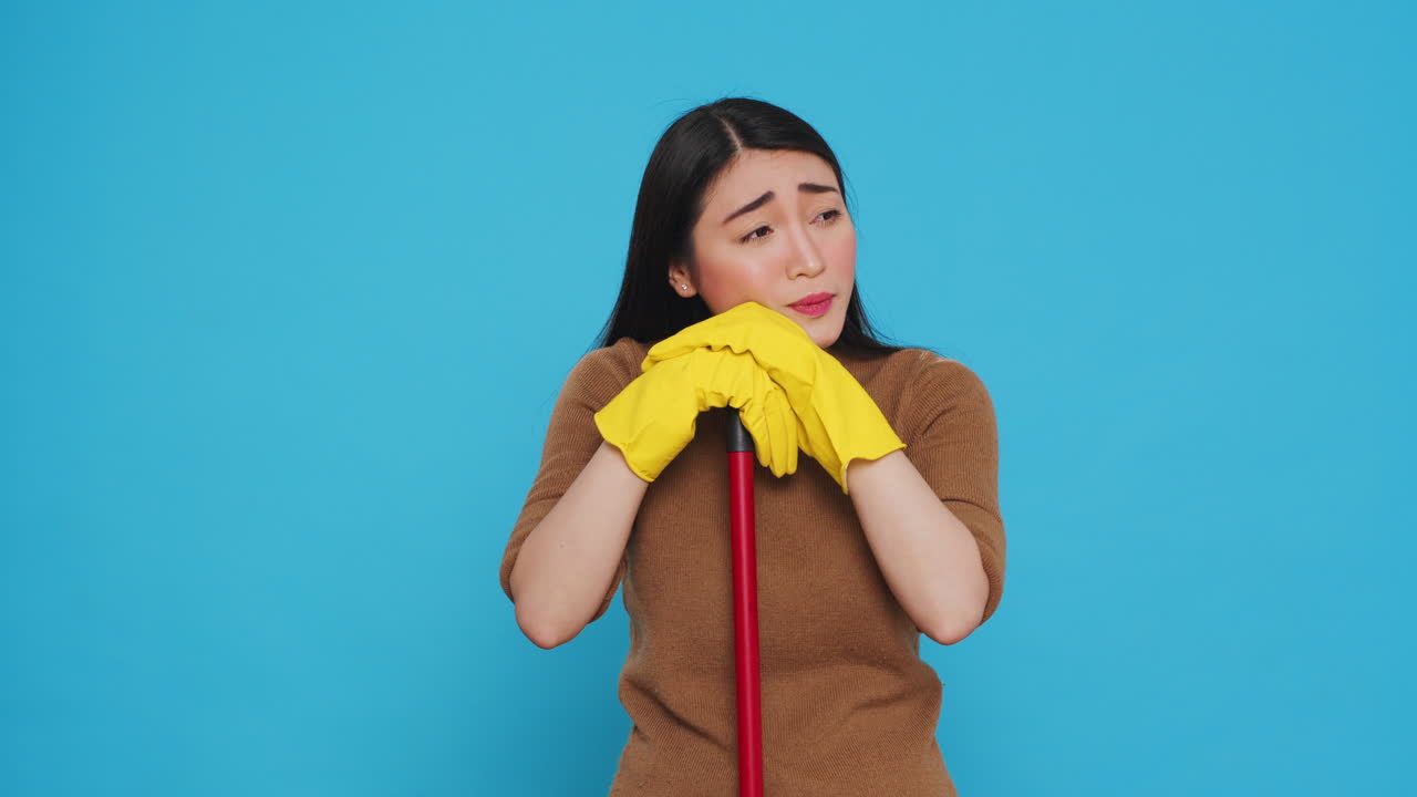 Tired housekepper falling asleep on broom while cleaning client home, being overworked in studio