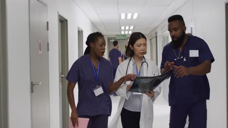 Video-of-three-diverse-male-and-female-doctors-walking-in-hospital-corridor-discussing-x-ray