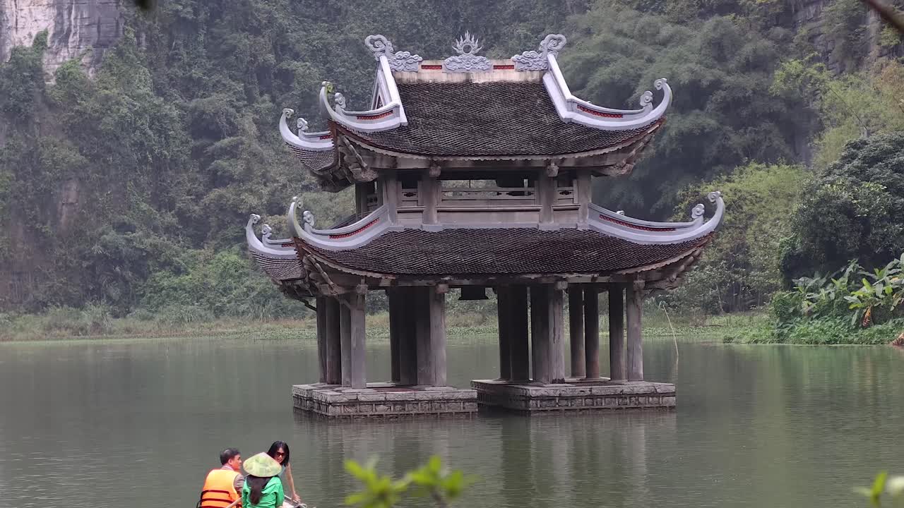 Tourists row boat near traditional pavilion