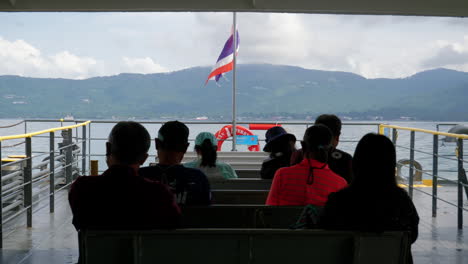 Reisende-Nehmen-Die-Fähre-Nach-Koh-Samui-Und-Beobachten,-Wie-Die-Thailändische-Flagge-Im-Windigen,-Bewölkten-Himmel-Weht