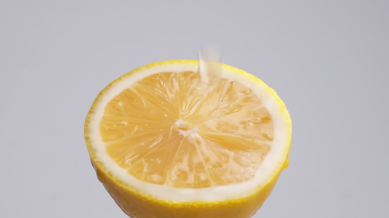 tiro macro de cámara lenta de agua que fluye de la rodaja de limón sobre fondo blanco