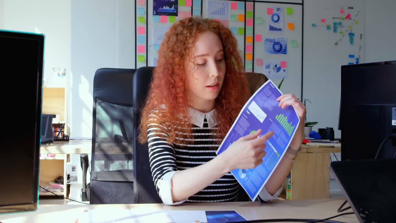 Forfra af ung, cool kaukasisk forretningskvinde, der sidder ved et skrivebord og kigger ind i kameraet på kontoret 4k