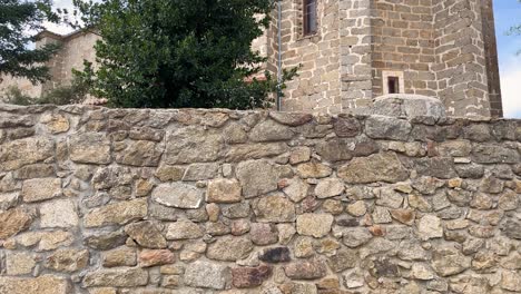 excellent filming with a camera elevation that begins with a good stone wall and then a beautiful holly tree appears and behind it the impressive sanctuary structure from the middle ages.