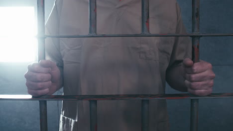 Medium-dolly-shot-of-a-prisoner-standing-at-the-door-to-his-cell,-holding-the-bars