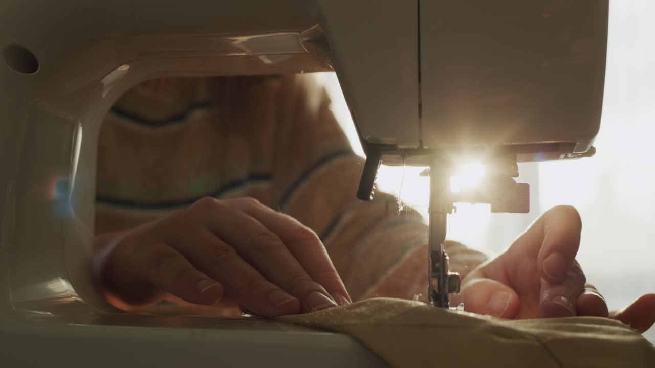 한 여자가 바느질기에서 침대 옷을  ⁇ 고 있습니다. 클로즈업입니다.