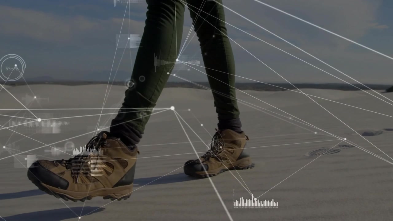 Mid adult hiker's boots walking dunes each step generating fitness data overlays with charts