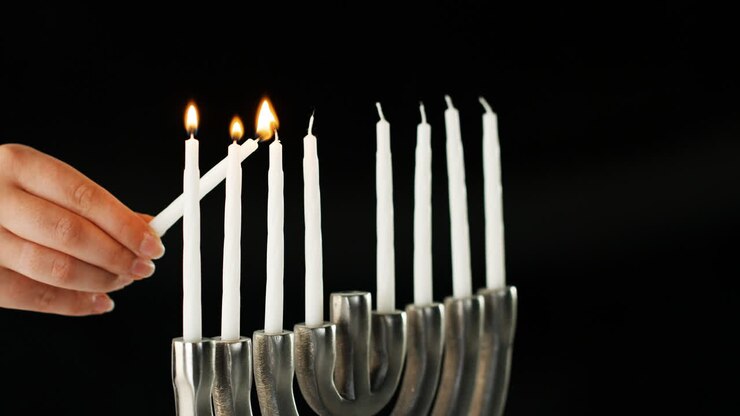 Hand lighting the nine white candles in a Jewish menorah sat on a pale marble surface, side view, close up detail