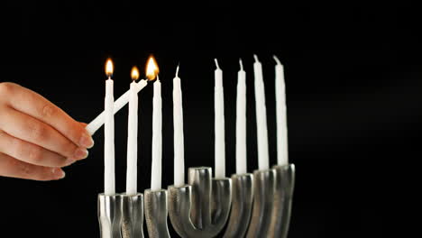 hand lighting the nine white candles in a jewish menorah sat on a pale marble surface, side view, close up detail