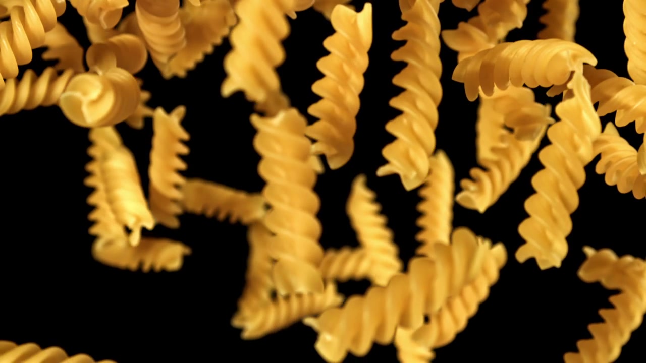 Pasta fusilli cruda che cade al rallentatore su sfondo nero