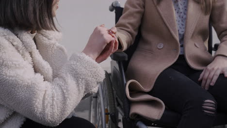 close up view of young woman talking with her disable friend holding her hand in a bar terrace