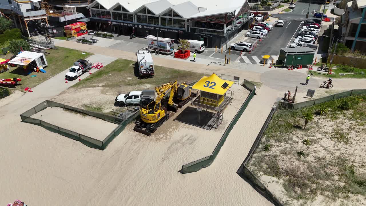 Aerial view of construction vehicles and workers on a beach, highlighting ongoing repair work under clear daylight