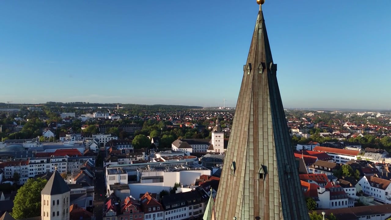 Vertical drone ascent climbs past the cathedral clock, roof structures and small turrets before tilting toward the twin crosses above.