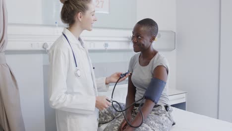 happy diverse female soldier patient and doctor measuring blood pressure in hospital, in slow motion