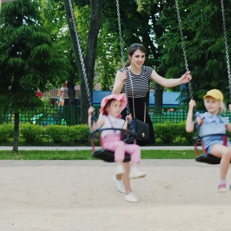 young mother pushes two daughters on a swing in a park