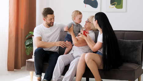 padres felices y abuela jugando con un niño sentado en un sofá en la sala de estar 1