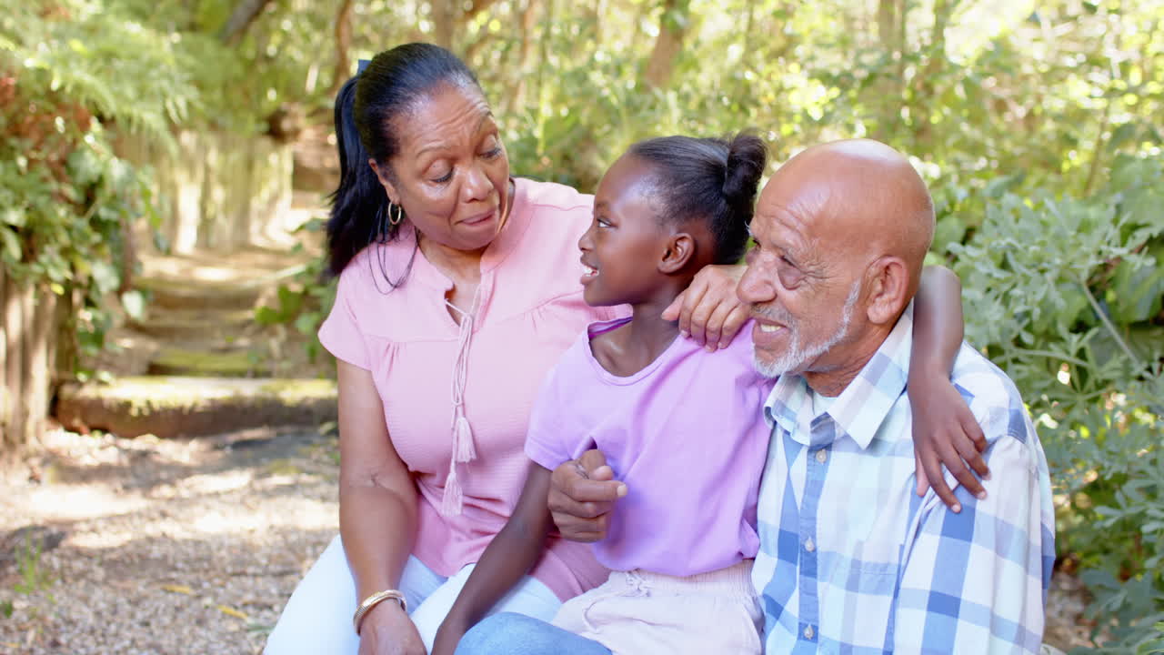 Diverse grandparents with granddaughter in garden, spending quality time smiling and laughing